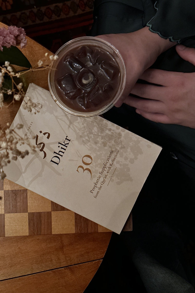 Dhikr on a café table beside a coffee and delicate flowers