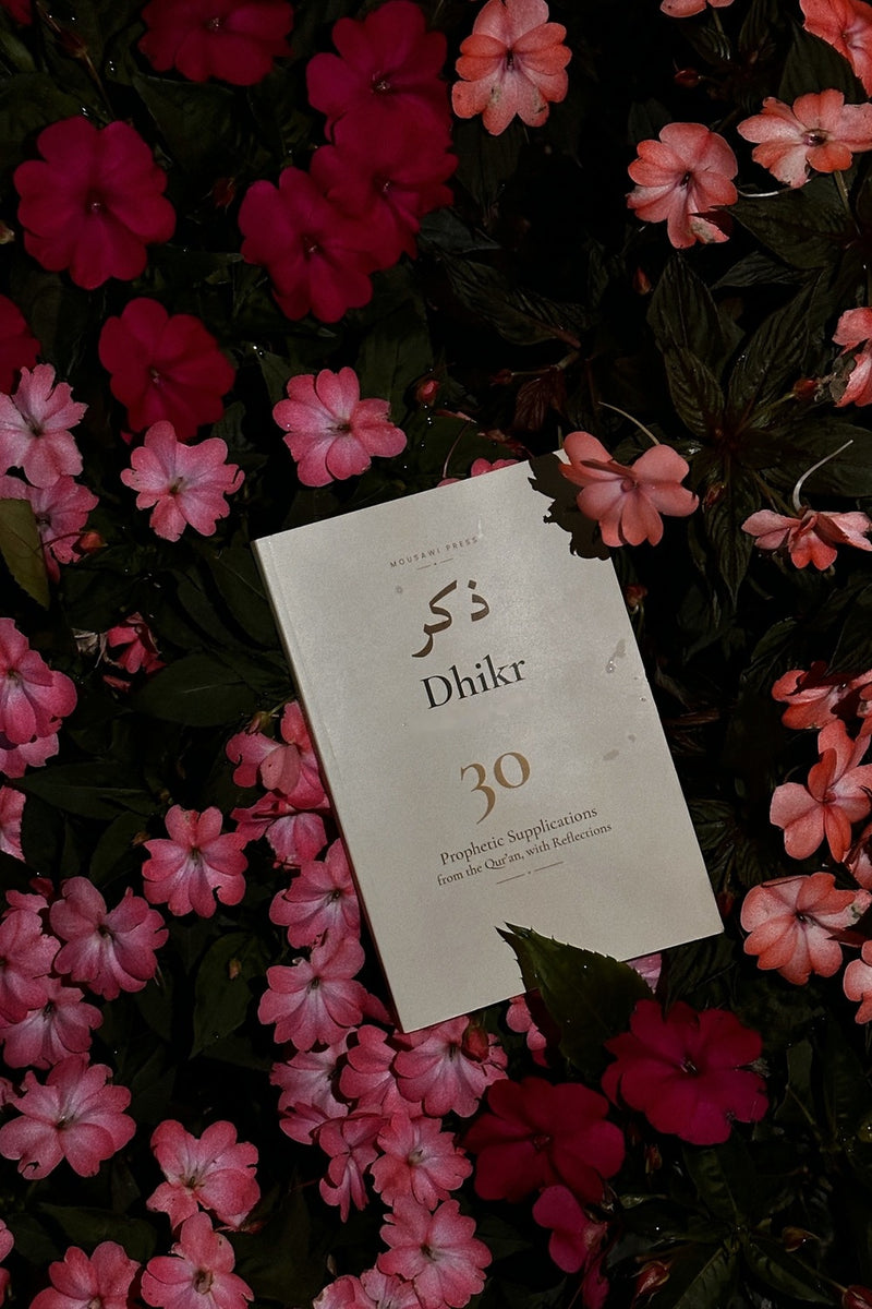 The cream cover of Dhikr nestled among pink and red flowers