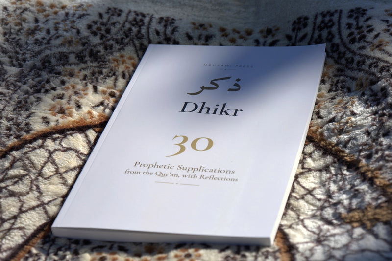 The cream front cover of Dhikr on a patterned rug